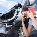 Woman On The Phone After Car Accident That Left Front Car Damage